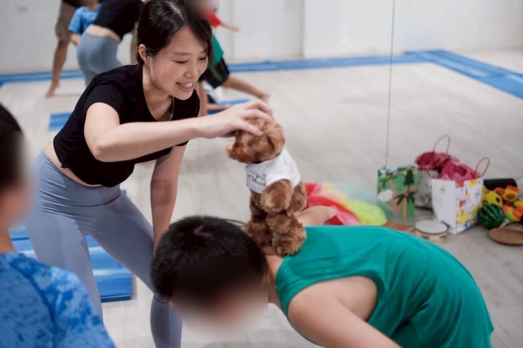 沛沛老師在兒童瑜伽課中，把小熊玩偶放在趴著的孩子背上玩平衡遊戲